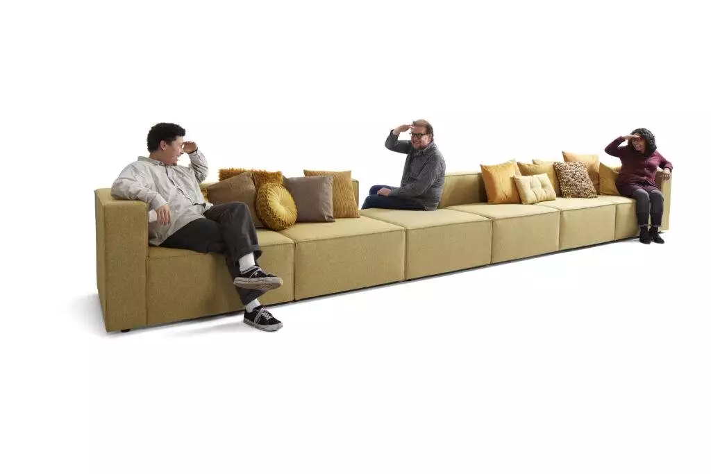 Drie mensen kijken naar elkaar op een lange loungebank met sierkussens.