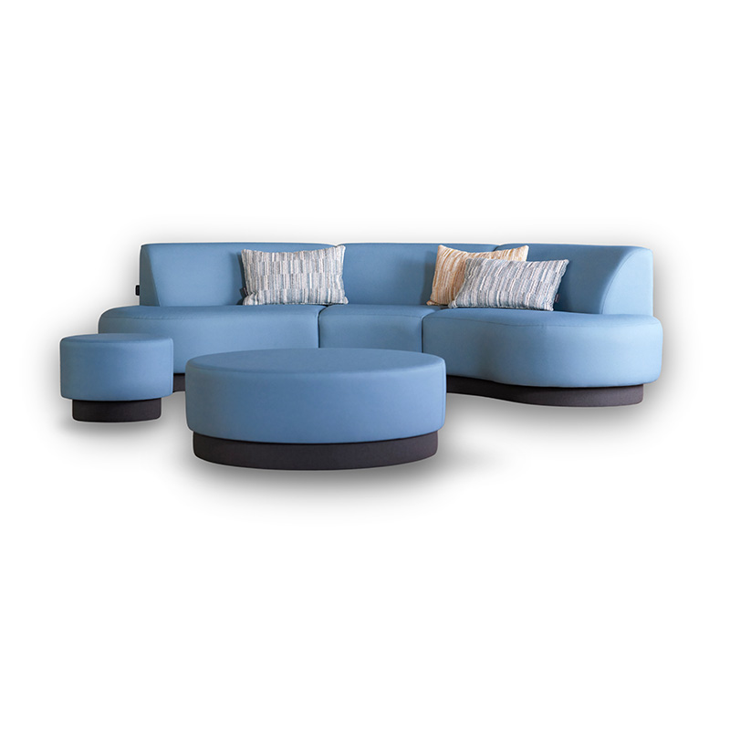 Bank Aline van Davant in lichtblauwe stoffering, met afgeronde zitdelen en bijpassende ronde poef, gefotografeerd vrijstaand op witte achtergrond.