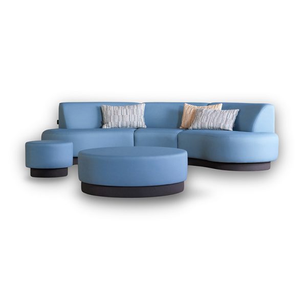 Bank Aline van Davant in lichtblauwe stoffering, met afgeronde zitdelen en bijpassende ronde poef, gefotografeerd vrijstaand op witte achtergrond.